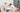 Alt text: Two young children standing on wooden Montessori learning towers while baking together at a kitchen table.